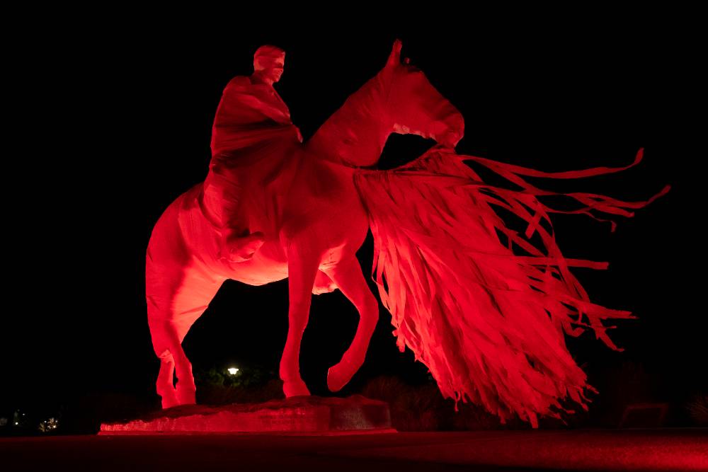 The Will Rogers and Soapsuds statue illuminated in red lights against a night sky