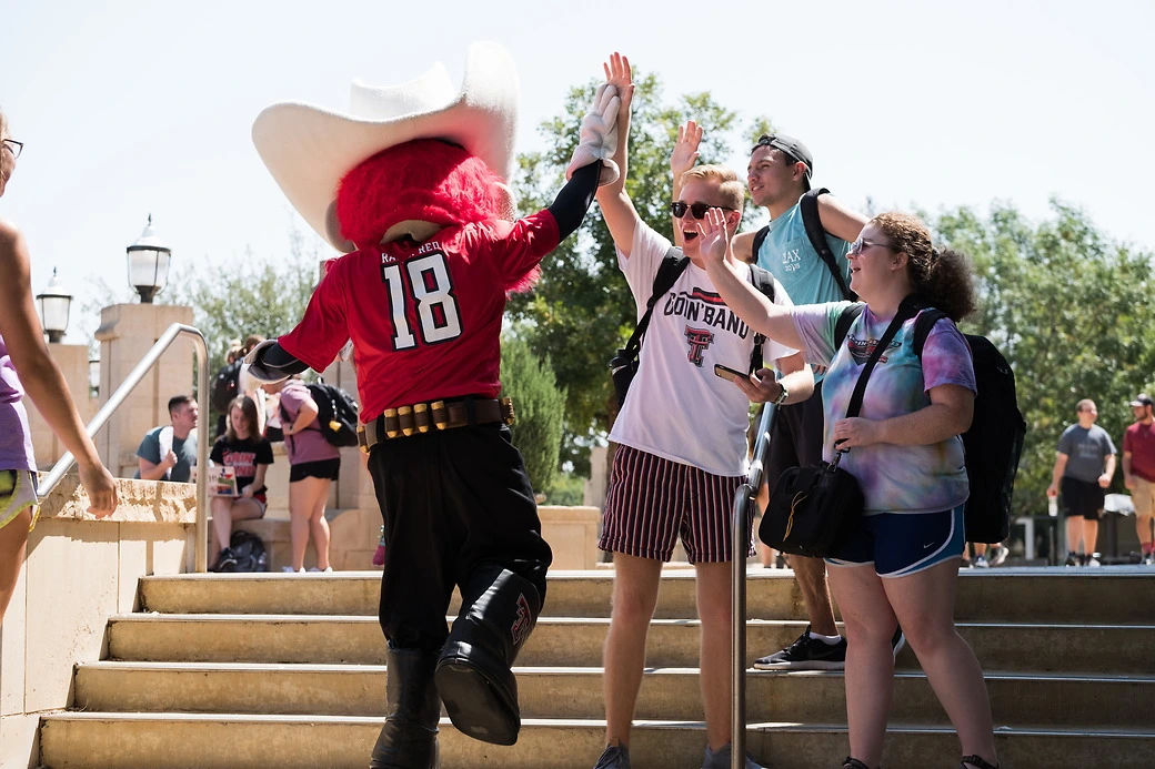 Three students doing high-fives with the Red Raider