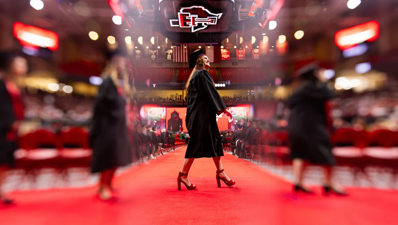 A graduate in cap and gown walking the red carpet at commencement