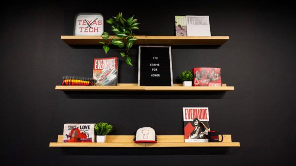 Wood shelves on a black wall, holding an assortment of Texas Tech merch and publications.