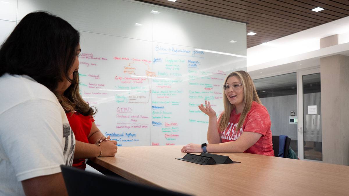 Photo of a woman talking to students with a whiteboard in the background.
