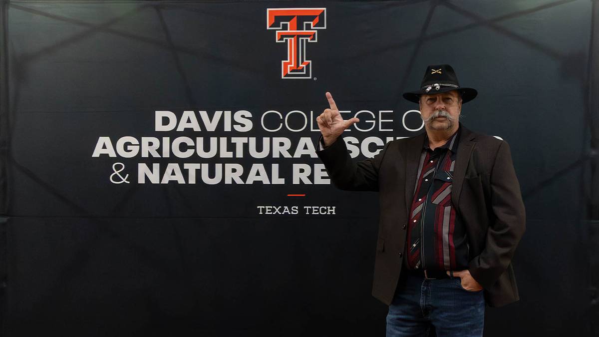 Robert Mason giving the Guns Up hand gesture in front of a banner for Davis College.