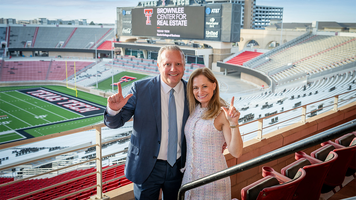 John and Rachel Brownlee standing in the Texas Tech football stadium holding their thumb and pointer finger in the 