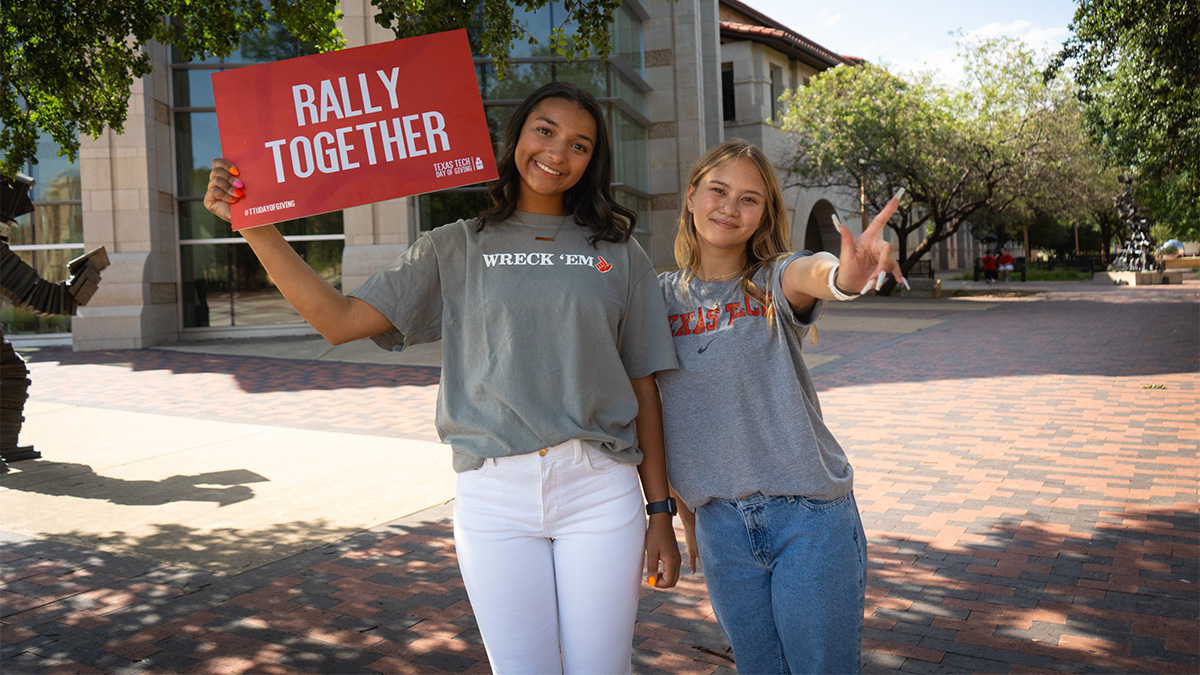 Two Texas Tech students standing outside. One is holding a sign that says 