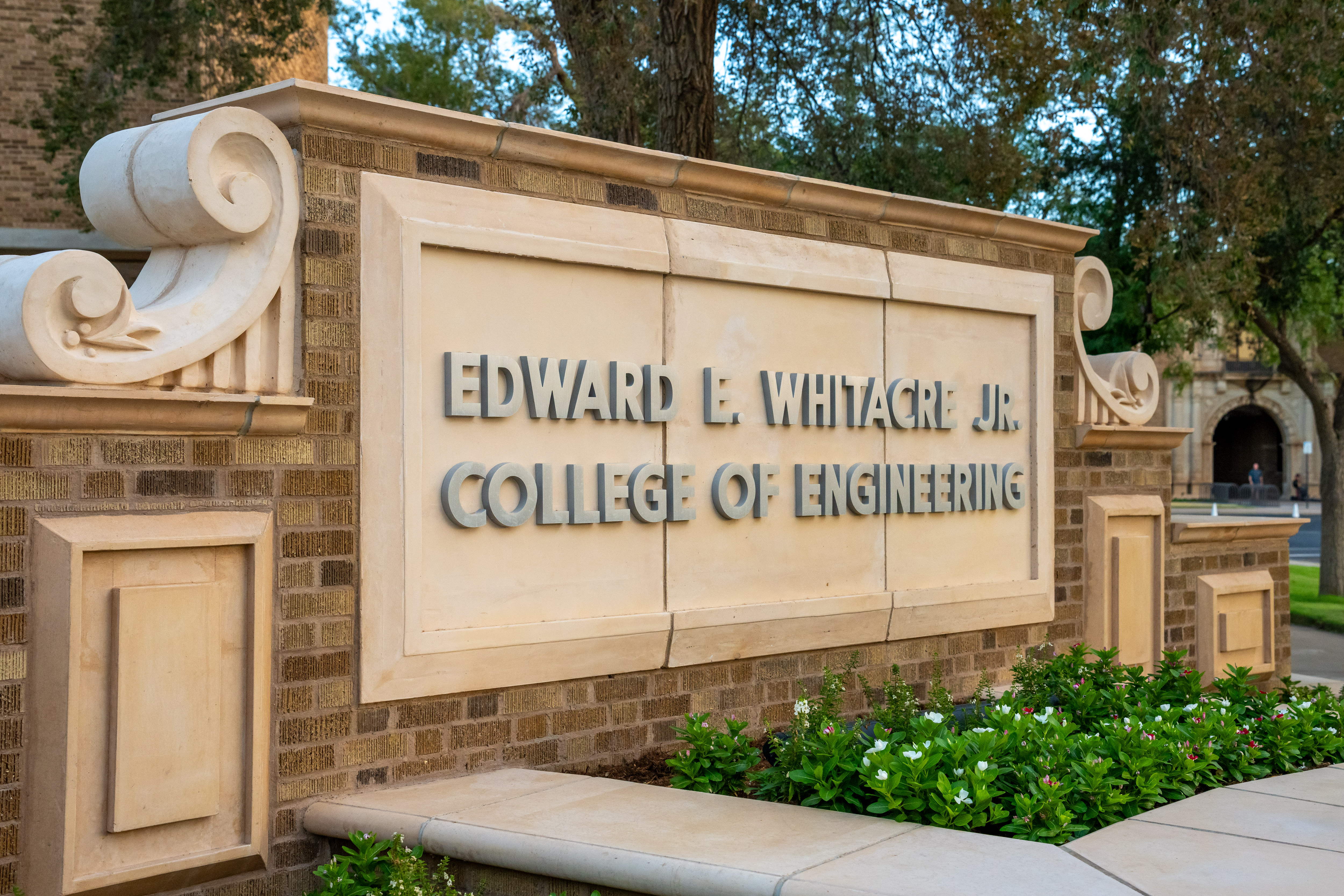 The exterior sign for the Edward E. Whitacre Jr. College of Engineering at Texas Tech University, framed by flowering shrubs and trees.