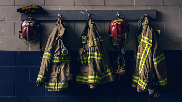 Firefighter helmets and turnout gear hang on hooks along a fire station wall