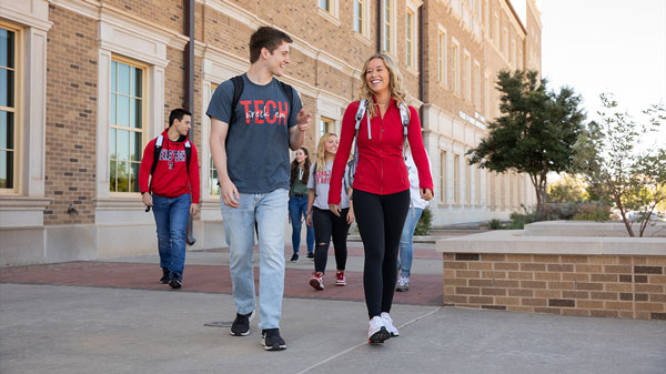 Texas Tech students wearing backpacks walk and talk together outside a campus building