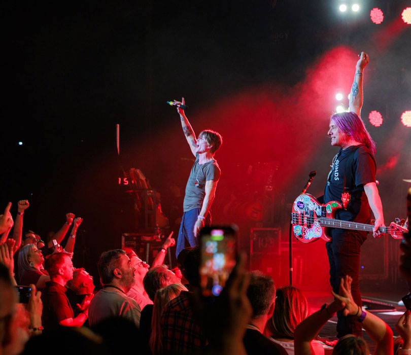 Members of the Goo Goo Dolls perform onstage as fans cheer and raise their hands during a live concert