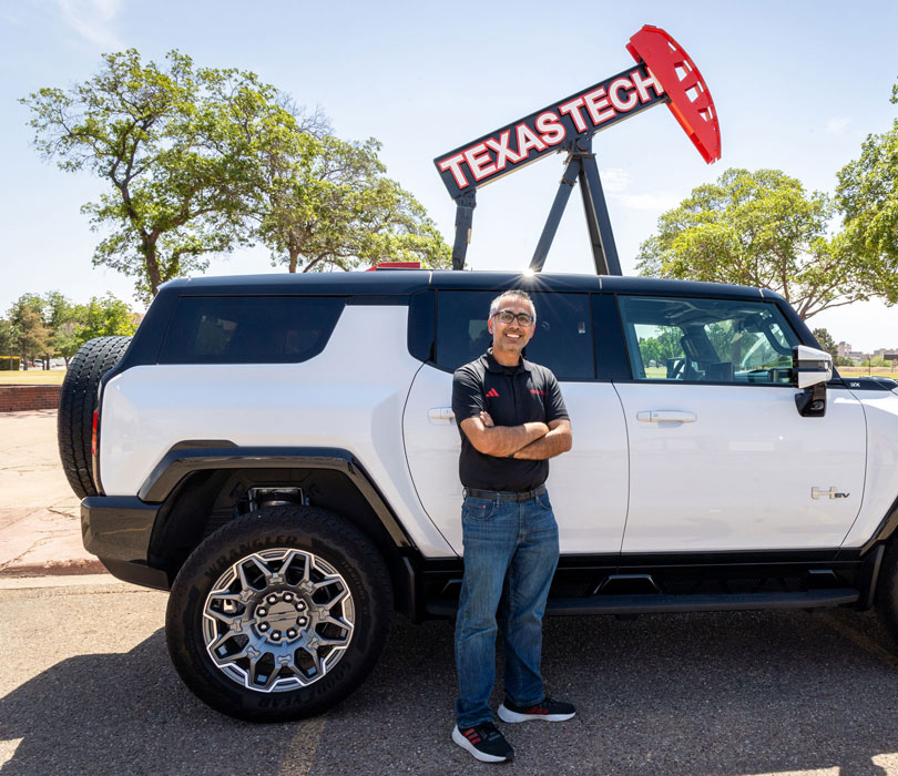 Ravi stands beside a white GMC Hummer EV parked beneath the university's iconic pumpjack sculpture.