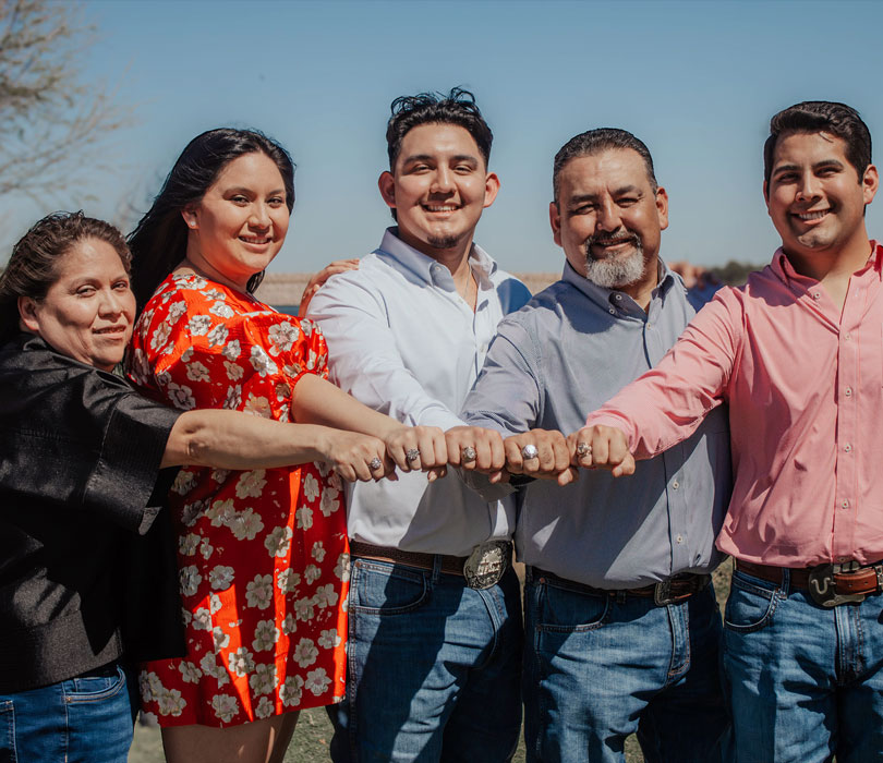 Five people stand outdoors, smiling and extending their fists together.
