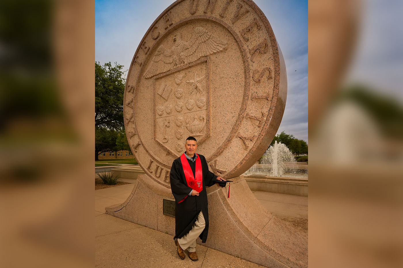 Rafael Morales standing in graduation gown at the Texas Tech University seal