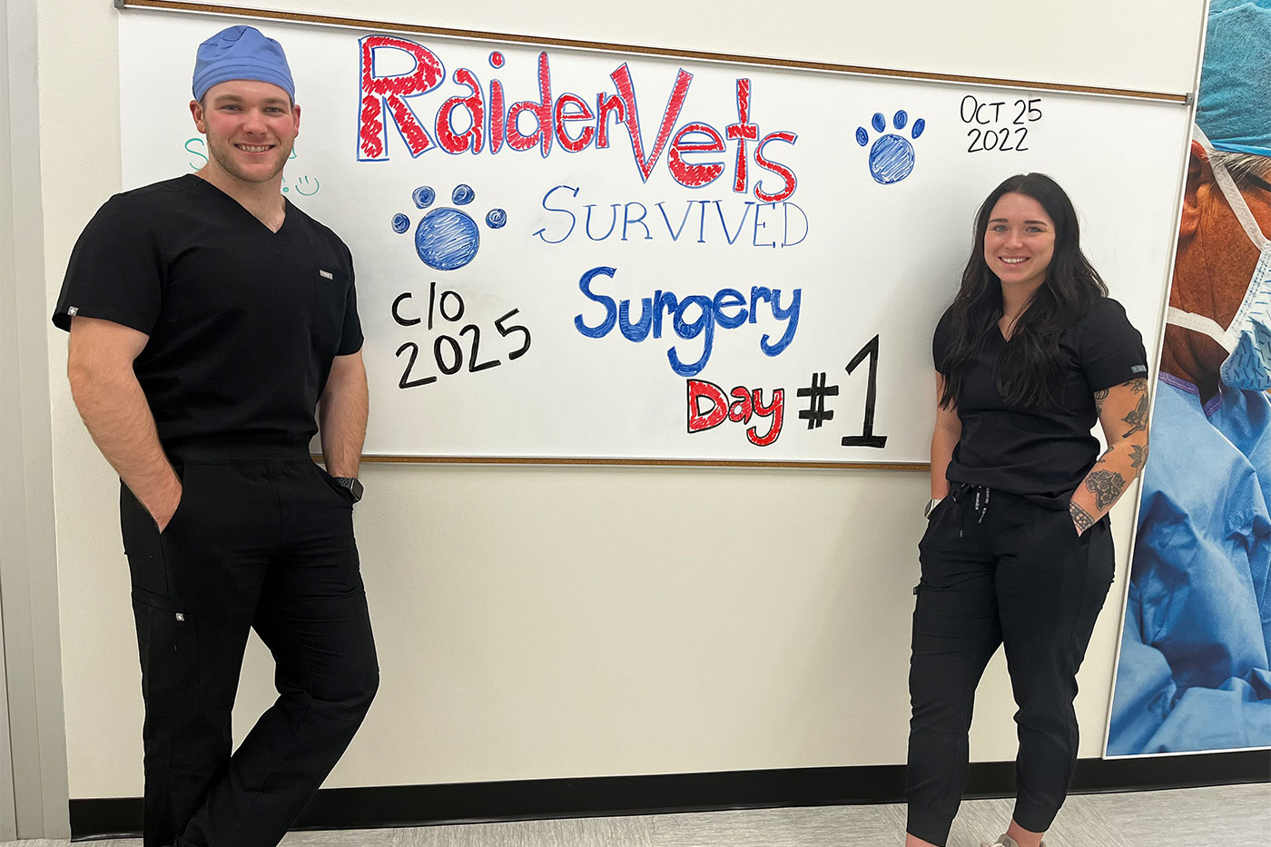 Austin and classmate stand in front of sign that reads "RaiderVets survived surgery day #1."