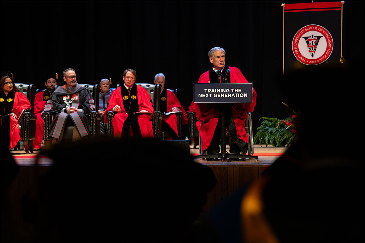 Governor Greg Abbott at the podium as Chancellor Emeritus Robert Duncan and Dean Guy Loneragan look on with the rest of the stage party.
