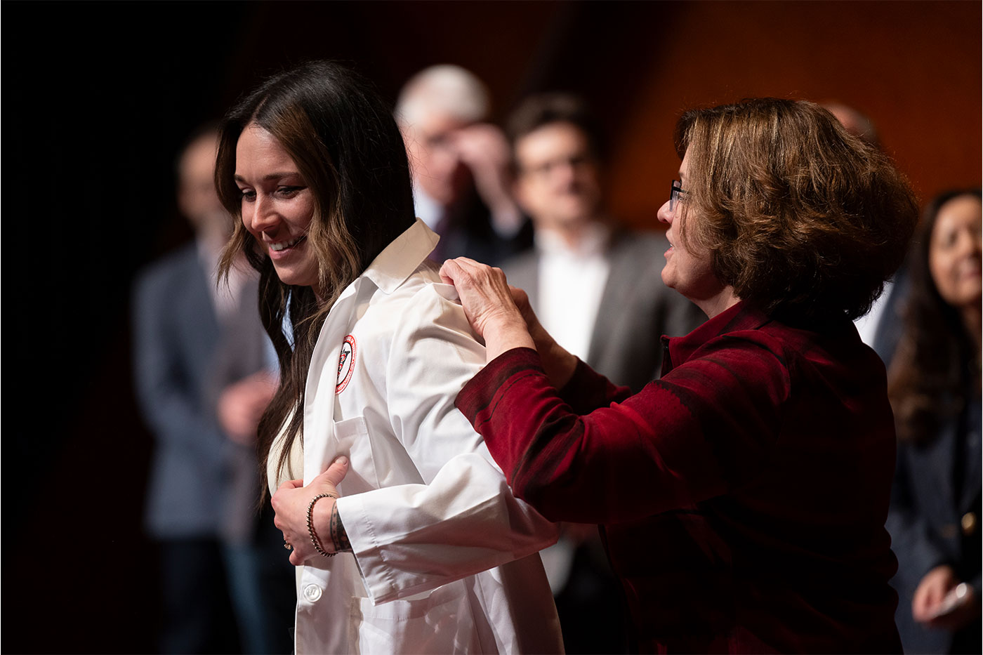 Woman helping female student put on her white coat.