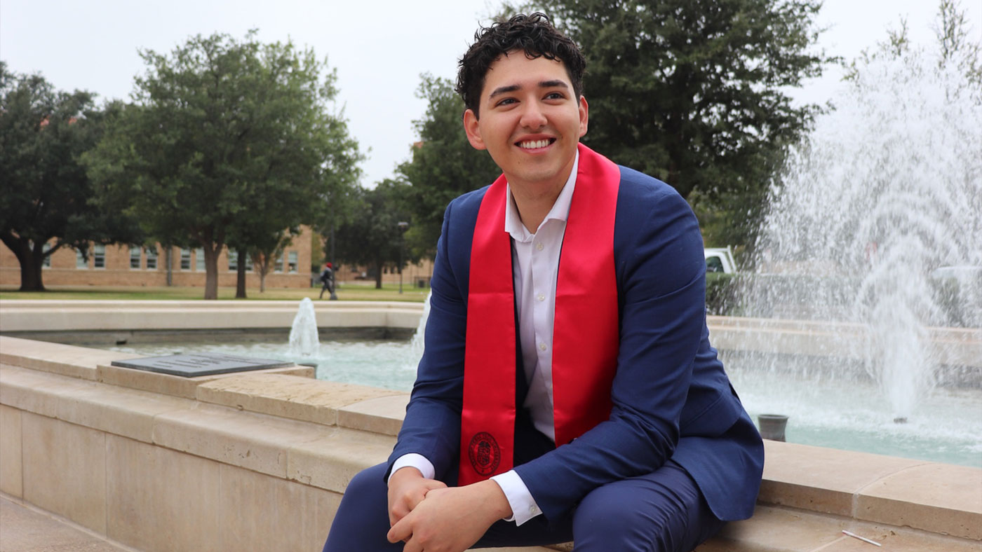 Roque wearing his commencement stoll while sitting in front of a fountain. 