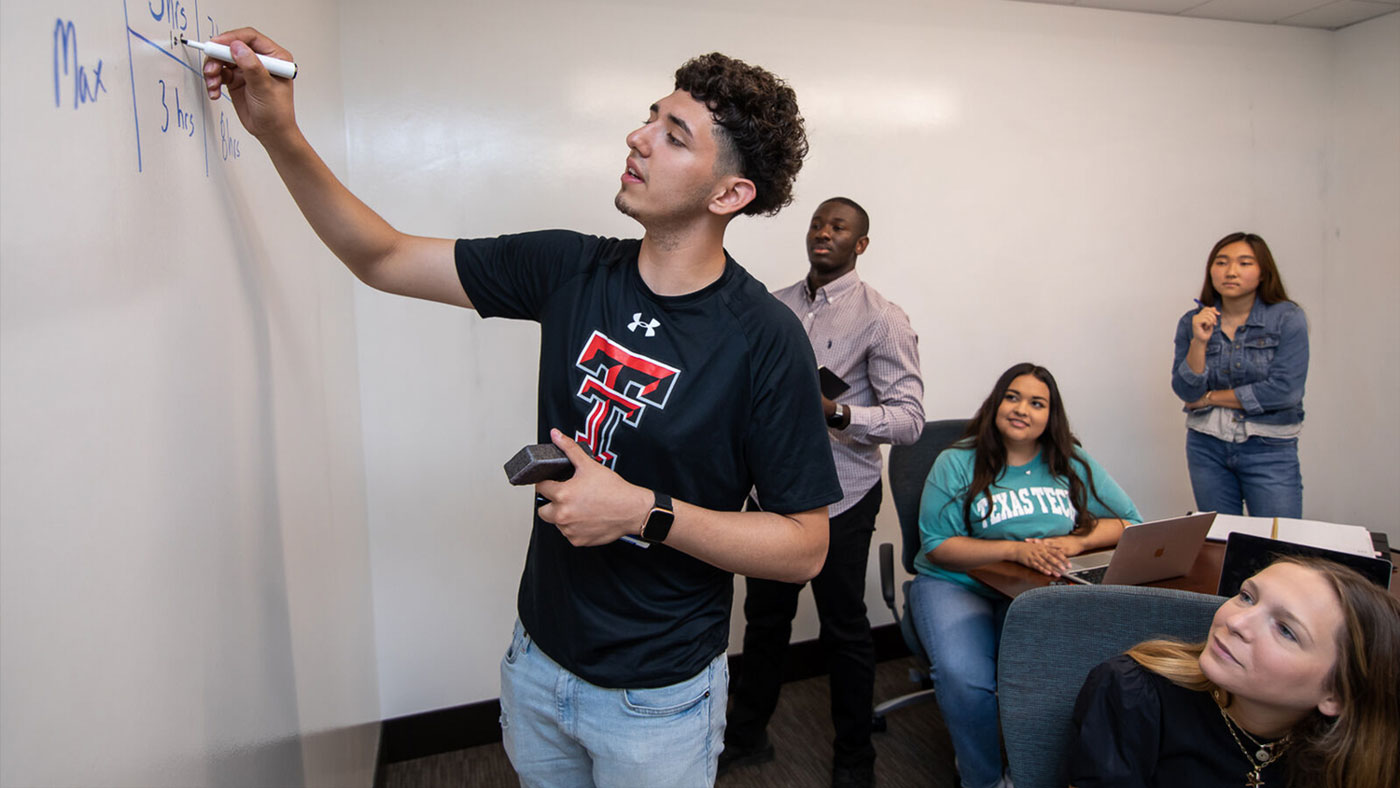 Roque writing on a dry erase board as other students watch. 