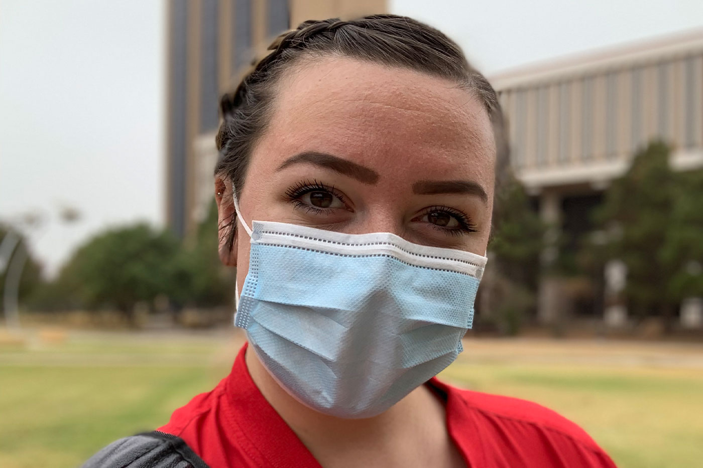 Gini wearing a COVID mask, standing in front of the College of Media and Communication. 