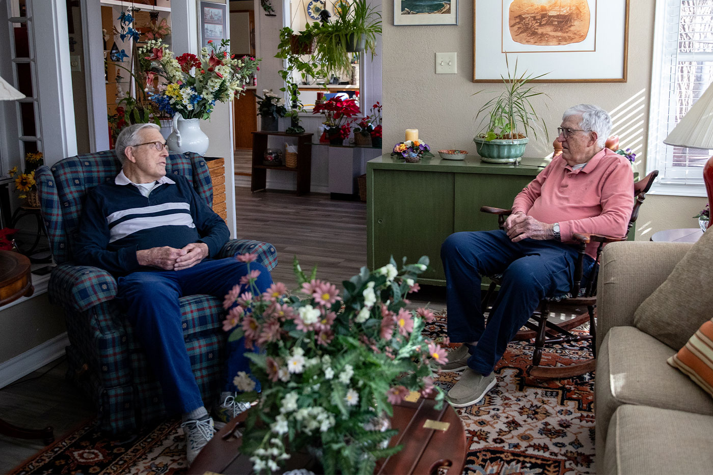 The brothers sitting in a living room with art and flowers everywhere. 