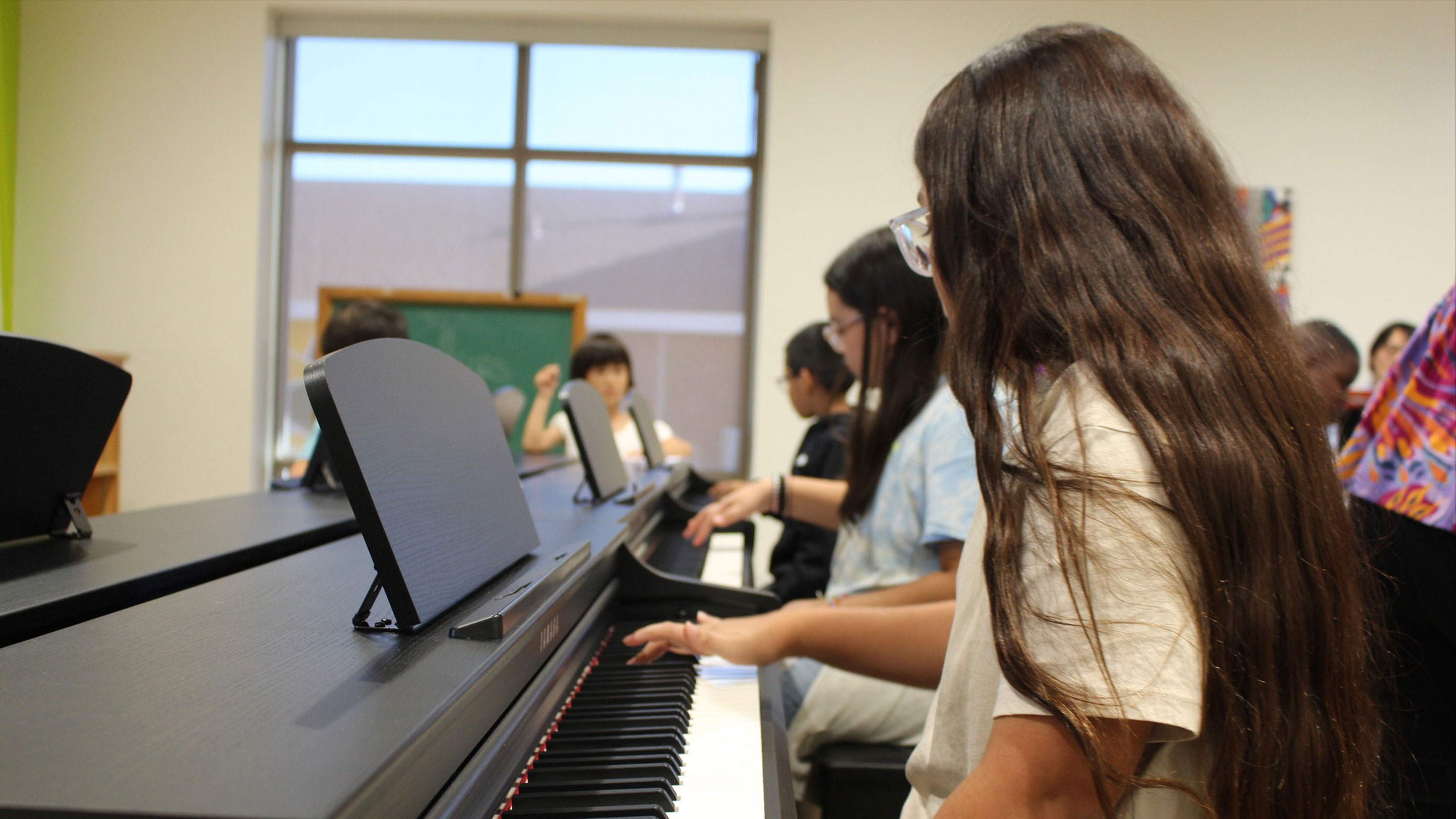 Children sitting at a row of pianos. 