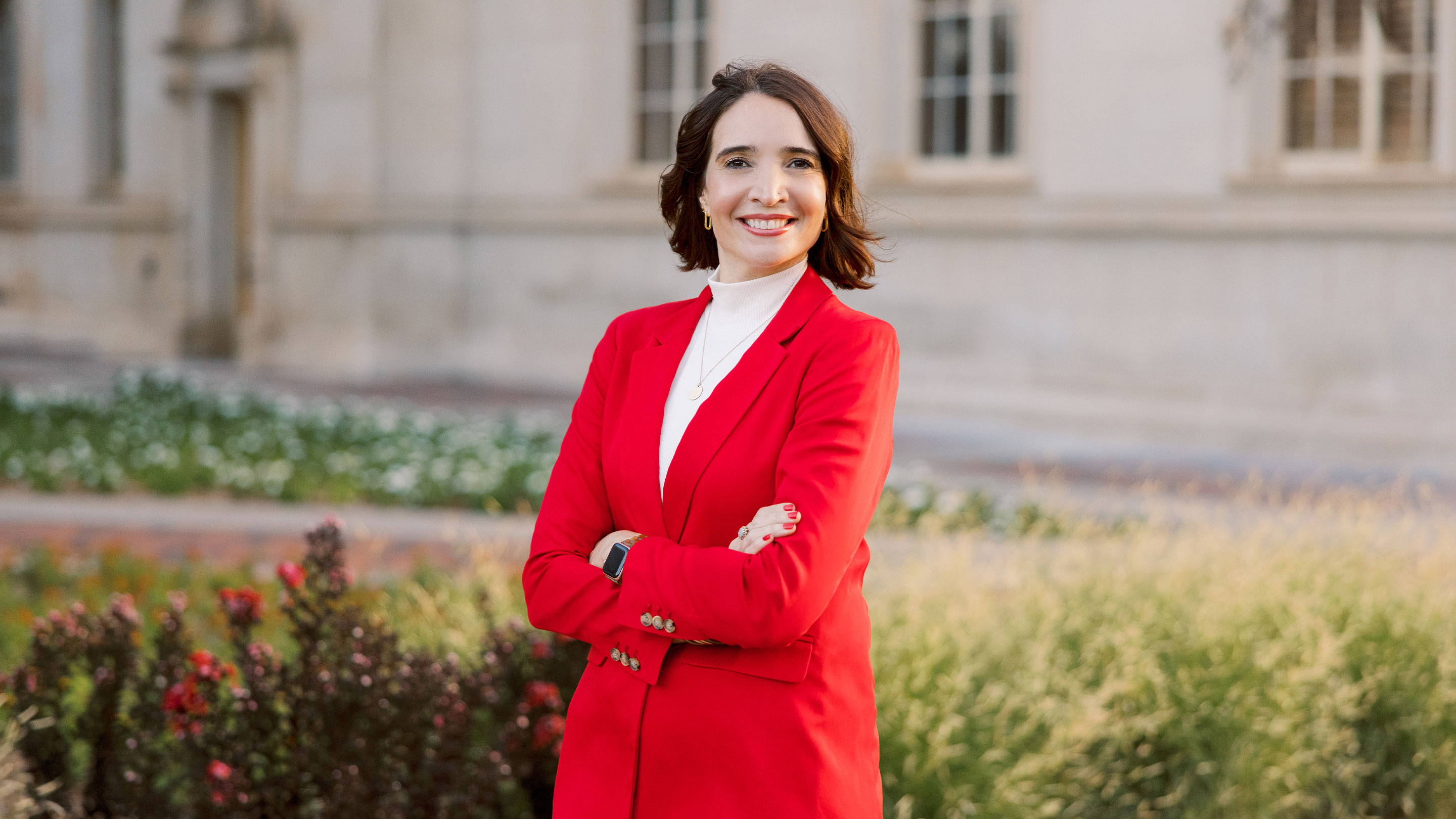 Sarai Brinker smiling and standing in a garden with arms crossed.