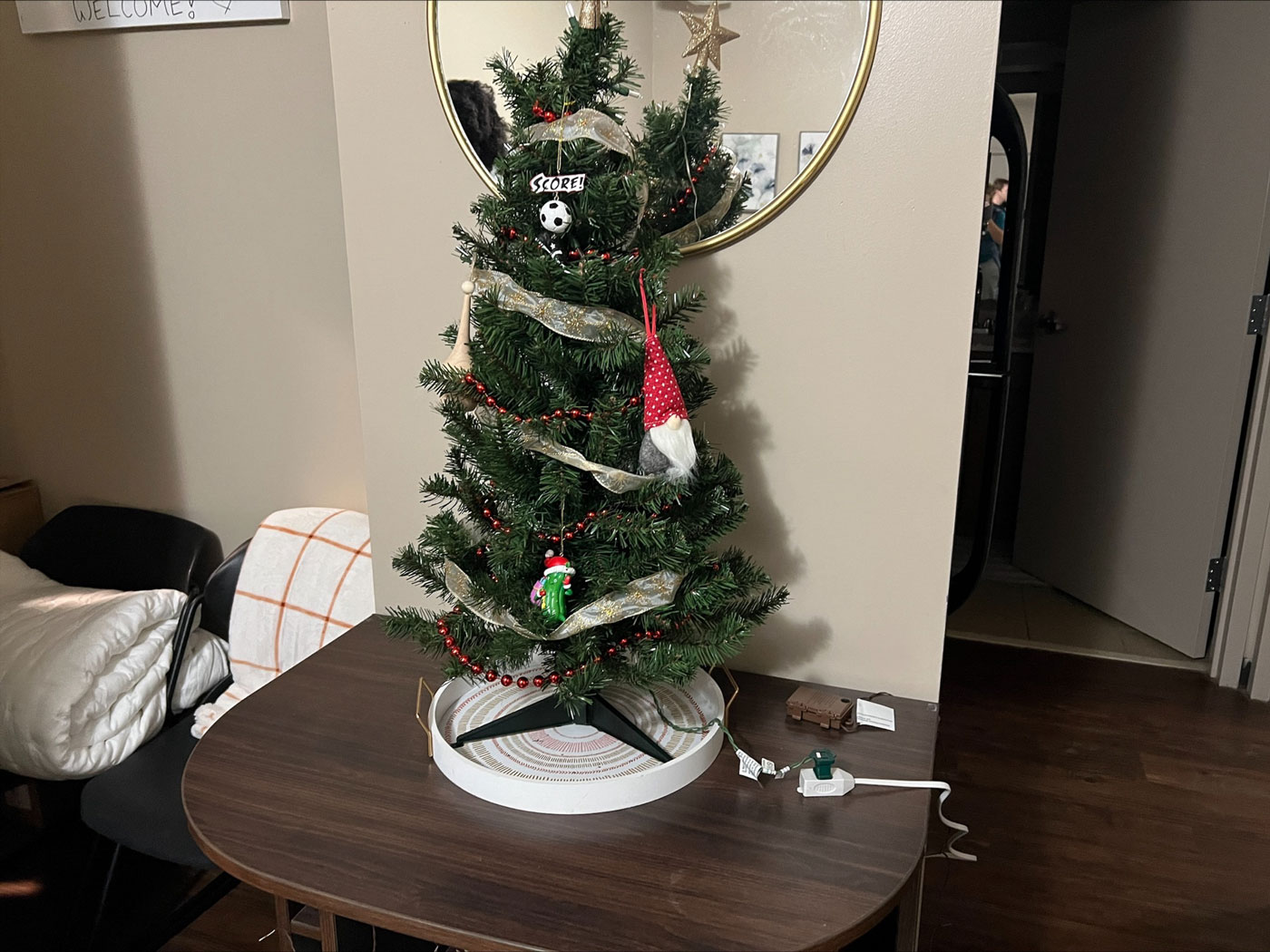 Small Christmas tree sitting on dorm room end table, with prohibited extension cord. 