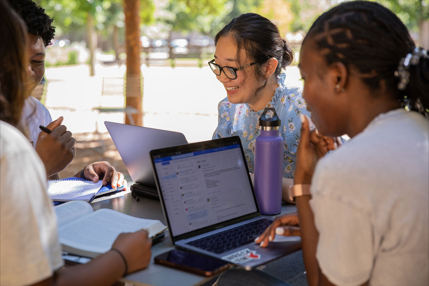 Girls of various ethnicities using laptop computers at an outdoor table.