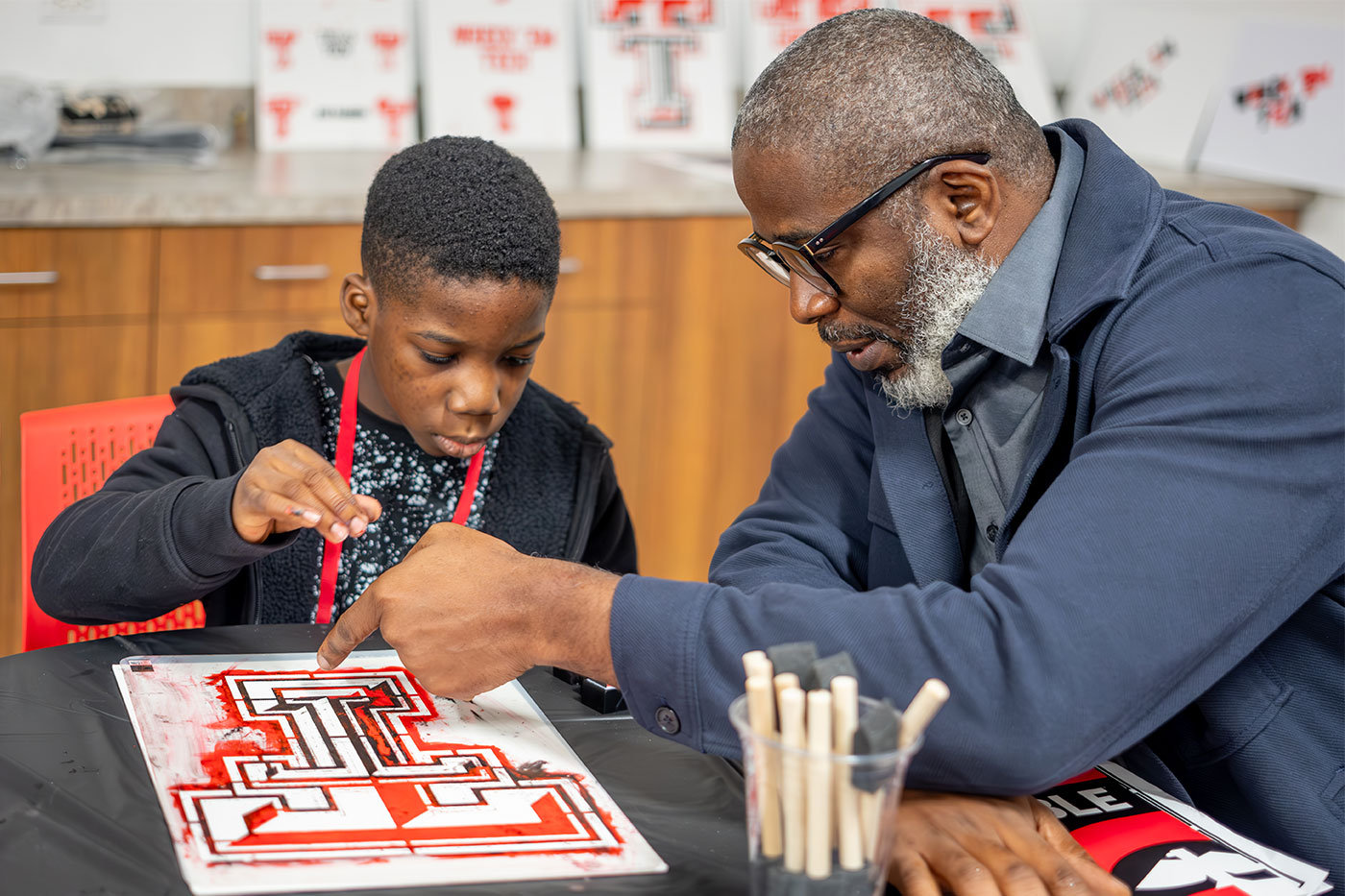 Father and son sit at a table painting a Double-T.