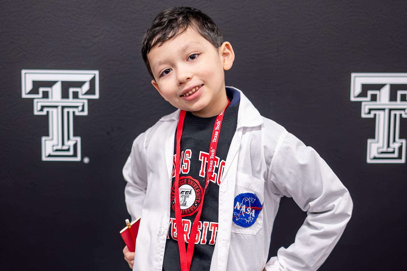 Young boy wearing a TTU shirt, lanyard and a white coat with NASA patch. 