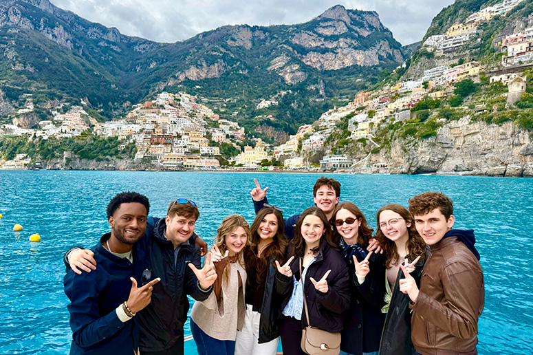 Group of students in a valley surrounded by a mountain village in the distance.