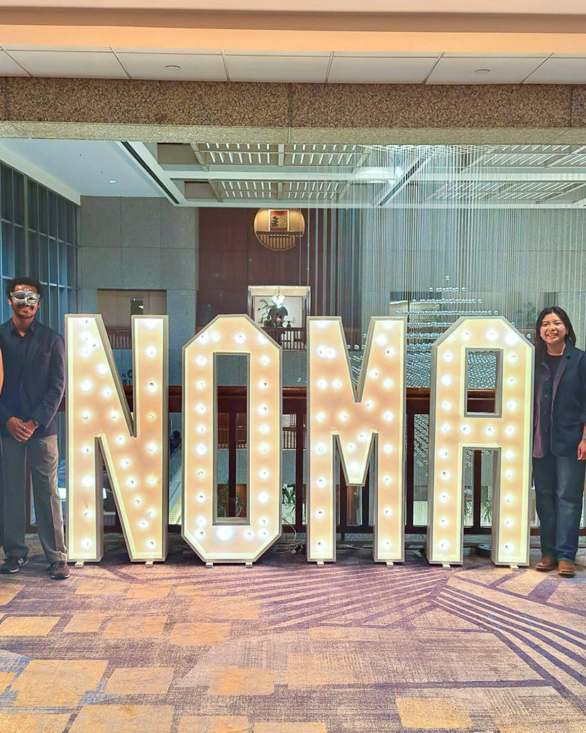 NOMAS members standing beside life-sized letters spelling out N-O-M-A-S.