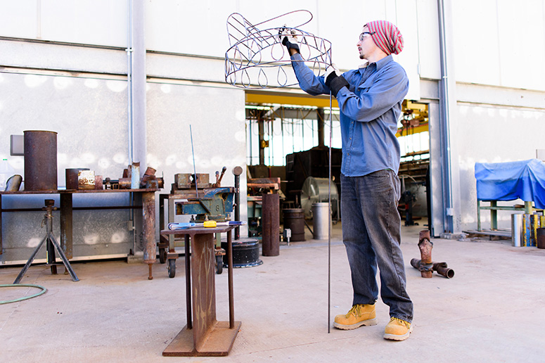 Male student adjusting sculpture outside.