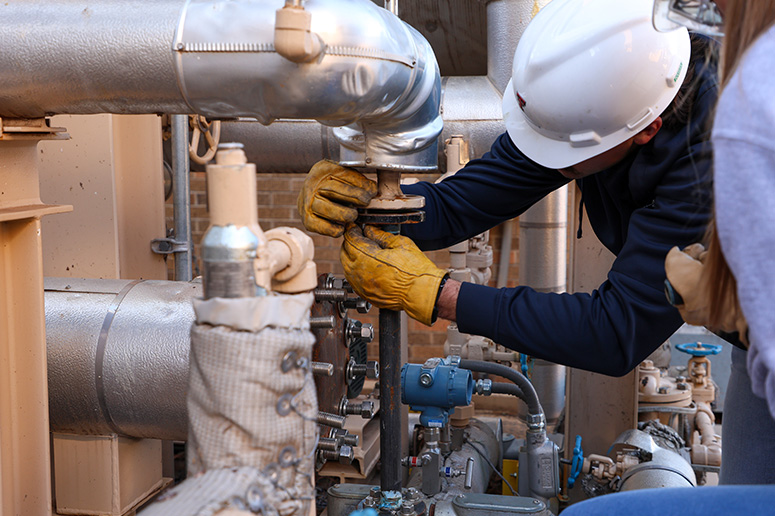 male with safety equipment working on chemical pipes